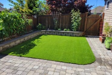 Backyard with synthetic turf and a stone patch wrapped around half of it in a curve