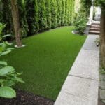 Backyard with synthetic turf and a stone pathway leading to a door on the right.