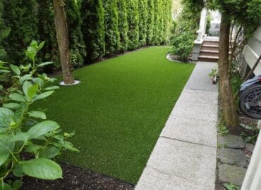 Backyard with synthetic turf and a stone pathway leading to a door on the right.