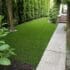 Backyard with synthetic turf and a stone pathway leading to a door on the right.